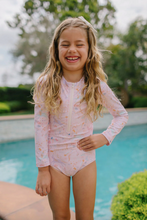 Load image into Gallery viewer, Young girl in a pink swimsuit standing by a pool with greenery in the background
