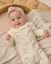 Load image into Gallery viewer, Baby in a cream-colored outfit with patterns, wearing a pink headband, lying on a textured beige blanket.
