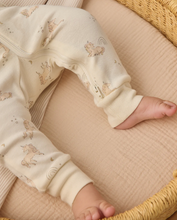 Load image into Gallery viewer, Baby's legs in cream-colored pants with animal prints on a textured surface.
