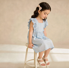 Load image into Gallery viewer, Young girl in a light blue dress sitting on a stool against a beige background
