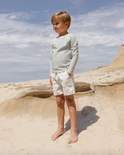 Load image into Gallery viewer, Child standing on a sandy landscape with a blue sky
