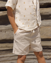 Load image into Gallery viewer, Person wearing a beige outfit with a patterned shirt and shorts on a stone background
