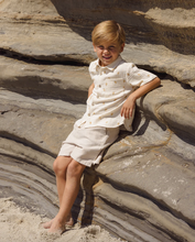 Load image into Gallery viewer, Child in a white outfit sitting on sandstone rocks
