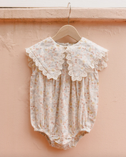 Load image into Gallery viewer, Floral baby romper with lace details on a wooden hanger against a peach background
