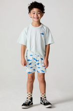 Load image into Gallery viewer, Child wearing a white t-shirt with a shark design, blue shorts with shark patterns, and black sneakers on a plain background.
