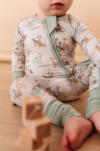 Load image into Gallery viewer, Child wearing a patterned onesie sitting on a wooden floor with wooden blocks.
