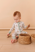 Load image into Gallery viewer, Baby in a light green and white outfit sitting on a wooden floor with toys.
