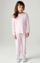 Load image into Gallery viewer, A young girl stands against a light gray studio background wearing a light pink long-sleeve pajama top and matching jogger pants, both printed with small white stars. She is also wearing white sneakers.
