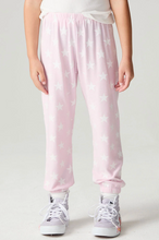 Load image into Gallery viewer, A child wearing light pink jogger-style pants with an allover white star pattern, paired with white sneakers, shown from the waist down against a plain light gray studio background.
