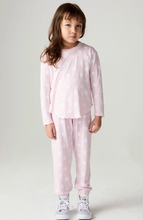 Load image into Gallery viewer, A young girl stands against a light gray studio background wearing a light pink pajama set with a white star pattern, consisting of a long-sleeve top and matching pants.
