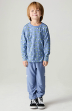 Load image into Gallery viewer, A young child standing against a light gray studio background, wearing a light blue long-sleeve top with a small repeating green and white print, matching light blue pants, and black low-top sneakers.
