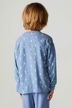 Load image into Gallery viewer, A child viewed from the back wearing a light blue long-sleeve pajama top with a repeating print of green dinosaurs and white lightning bolts, paired with matching light blue pants, against a plain light gray studio background.
