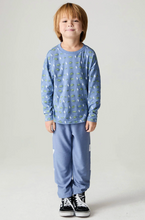 Load image into Gallery viewer, A young boy wearing a light blue long-sleeve pajama top with a green and white all-over print, paired with matching light blue sweatpants and black sneakers, standing against a plain light gray studio background.
