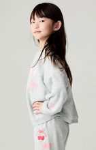 Load image into Gallery viewer, A young girl with long dark hair is shown in profile wearing a light gray heathered sweatshirt and matching sweatpants with pink bow and cherry embroidery, against a plain light gray studio background.
