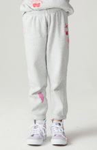 Load image into Gallery viewer, A person wearing light heather gray jogger sweatpants with pink graphic accents, paired with white sneakers, shown from the waist down against a plain light gray studio background.
