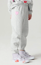 Load image into Gallery viewer, A child wearing light gray heather sweatpants with pink heart and cherry patches, paired with lavender high-top sneakers, shown from the waist down against a plain light background.
