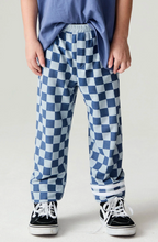 Load image into Gallery viewer, A child wearing blue and white checkered pants, a blue t-shirt, and black sneakers, standing against a light gray studio background.
