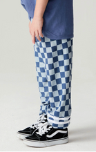 Load image into Gallery viewer, A child wearing blue and white checkered pants with a blue t-shirt and black low-top sneakers, shown from the waist down on a light studio background.
