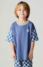Load image into Gallery viewer, A young boy wearing a blue short-sleeve t-shirt with blue and white checkered sleeves and matching checkered pants, standing against a light gray studio background.
