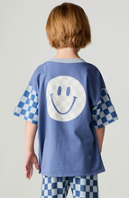 Load image into Gallery viewer, A child viewed from behind wearing a blue oversized T-shirt with a large white smiley face graphic on the back and blue-and-white checkered sleeves, paired with matching checkered pants, against a light gray studio background.
