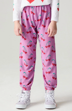 Load image into Gallery viewer, A child wearing pink jogger pants with a red cherry print, a white long-sleeve top with red heart graphics, and white sneakers, shown from the waist down against a light gray studio background.
