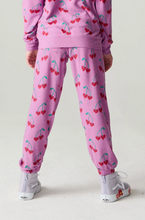 Load image into Gallery viewer, A child shown from the back wearing a pink zip-up sweatshirt and matching jogger pants with an allover red cherry print, paired with white sneakers, against a light gray studio background.
