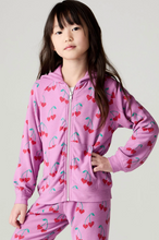 Load image into Gallery viewer, A young girl wearing a pink zip-up hoodie and matching sweatpants set with a red cherry and green stem pattern, posed against a light gray studio background.
