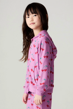 Load image into Gallery viewer, A young girl with long dark hair is shown in profile wearing a pink zip-up hoodie and matching pants set, both covered in a red cherry print with green stems, against a plain light gray studio background.
