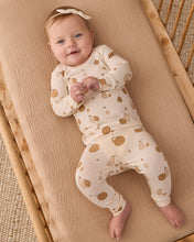 Load image into Gallery viewer, A baby lying on their back on a beige muslin blanket inside a wooden bassinet, wearing a cream-colored long-sleeve footed sleeper with a brown pumpkin and bunny print, along with a matching headband.
