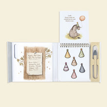 Load image into Gallery viewer, Open activity book showing Eeyore, six colorful party hats, Piglet’s party checklist, and the water pen in its holder.
