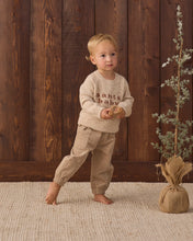 Load image into Gallery viewer, Barefoot child wearing latte tan pants with a cream “santa baby” sweater, holding a wooden toy.
