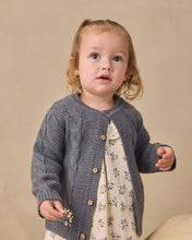 Load image into Gallery viewer, A toddler girl wearing a gray cable-knit cardigan over a cream floral dress, standing against a warm beige studio background.
