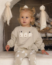 Load image into Gallery viewer, A young child wearing a light beige crewneck sweatshirt and matching pants with white ghost prints, sitting in front of a fireplace with Halloween ghost decorations hanging in the background.
