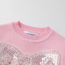 Load image into Gallery viewer, Close-up of a light pink knit sweater with a large sequined bow detail on the front, featuring a ribbed crew neck.
