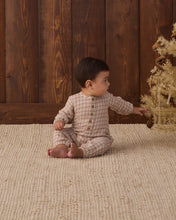 Load image into Gallery viewer, Baby wearing a Christmas plaid jumpsuit, seated on a cream rug and reaching toward a decorative tree.
