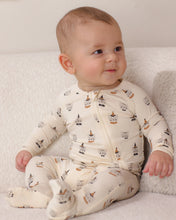 Load image into Gallery viewer, A baby sitting on a soft white textured surface wearing a cream-colored footed zip-up sleeper with a small gnome pattern.
