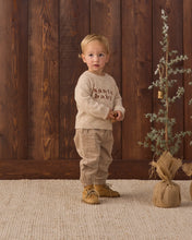 Load image into Gallery viewer, Child wearing latte tan pants with a cream “santa baby” sweater and tan boots beside a small Christmas tree.
