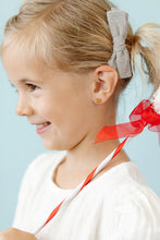 Load image into Gallery viewer, Smiling child wearing a gold-tone snowflake stud earring and a gray hair bow, holding a red-and-white striped wand.
