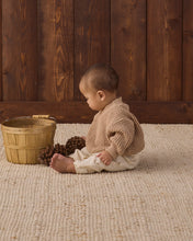 Load image into Gallery viewer, Side view of a seated baby wearing cream rocking-horse print pants with a tan knit sweater beside a wooden basket.
