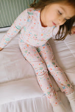 Load image into Gallery viewer, Overhead view of a child sitting on a bed in Sugar Plum pajamas, showing the matching printed top and pants.
