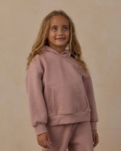 Load image into Gallery viewer, A young girl with long blonde hair wearing a dusty pink matching hoodie and sweatpants set, standing against a plain beige background.
