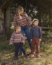 Load image into Gallery viewer, Three children wearing matching striped knit sweaters and jeans stand outdoors in front of a large tree trunk, with a woman standing behind them.
