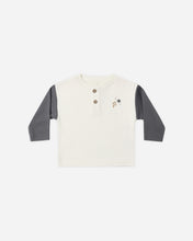 Load image into Gallery viewer, A toddler's long-sleeve henley shirt in off-white with dark gray sleeves, featuring a three-button placket and a small embroidered star and lightning motif on the left chest.

