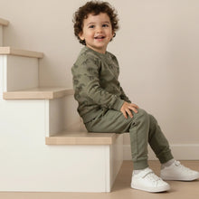 Load image into Gallery viewer, Child wearing a green outfit with white sneakers sitting on a staircase.
